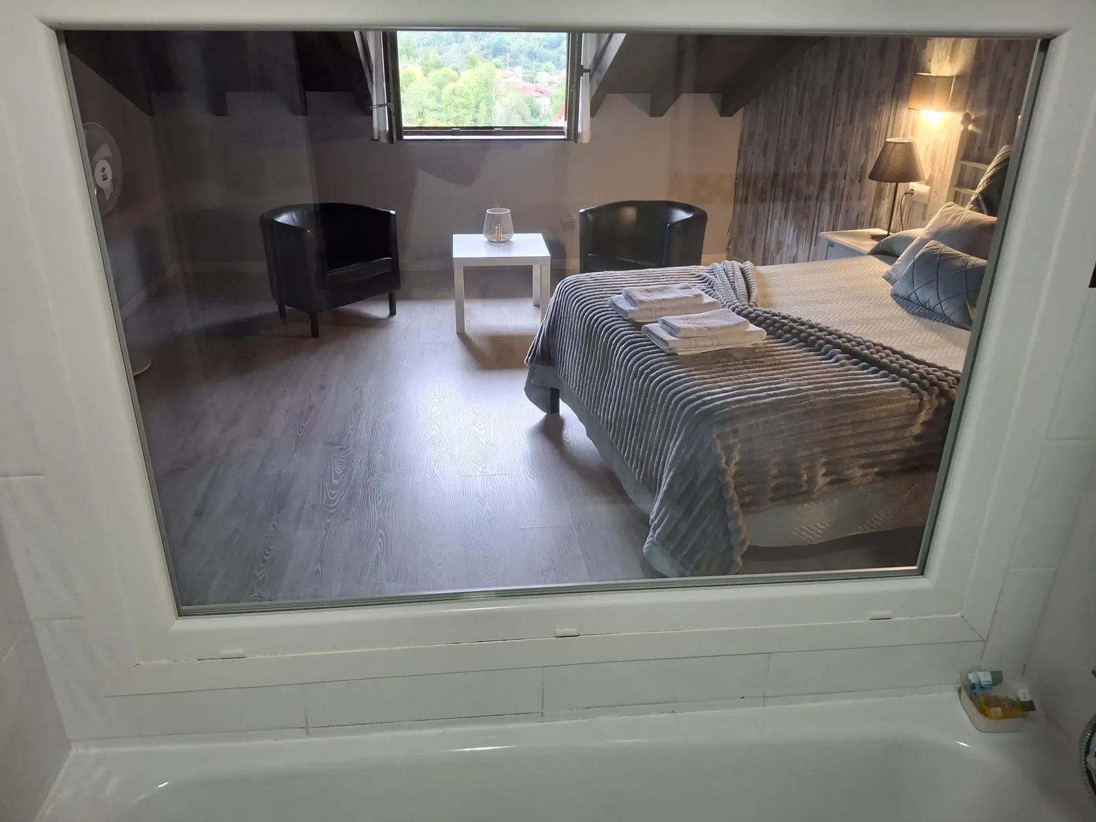 Bathtub in the upstairs bathroom of the Cares apartment, with a glass panel onto the bedroom and its window