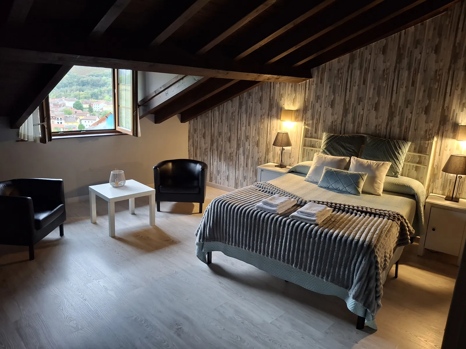 Dormitorio abuhardillado del apartamento Cares, con vigas de madera, sillones y ventana al valle