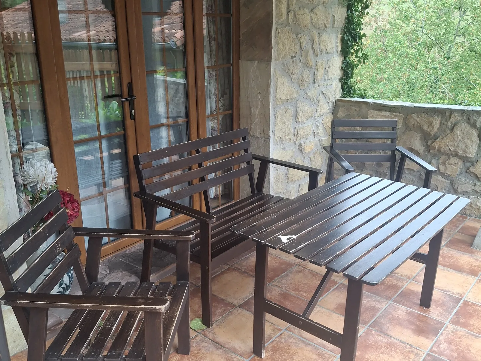 Porche de La Casina, con mesa y sillas de madera junto a las puertas del salón