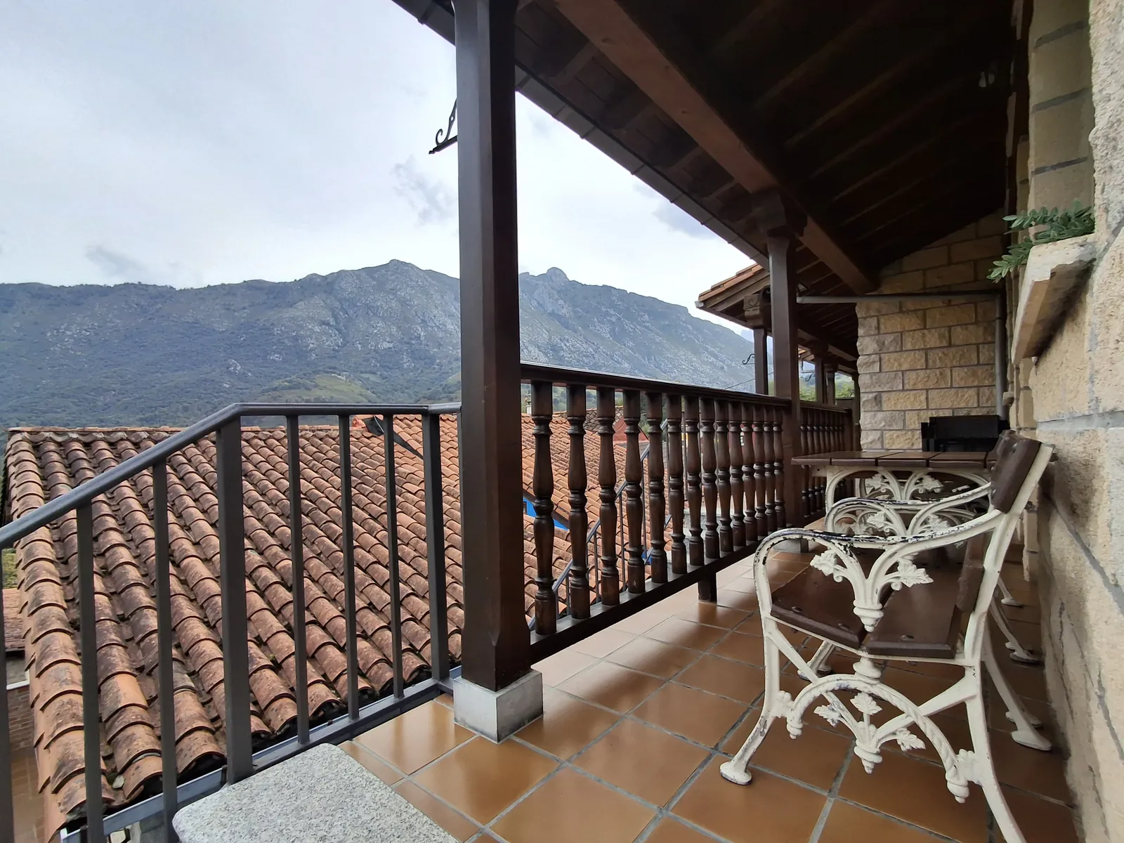 Galería cubierta común frente al apartamento Ribeles, con banco y mesa y la montaña al fondo